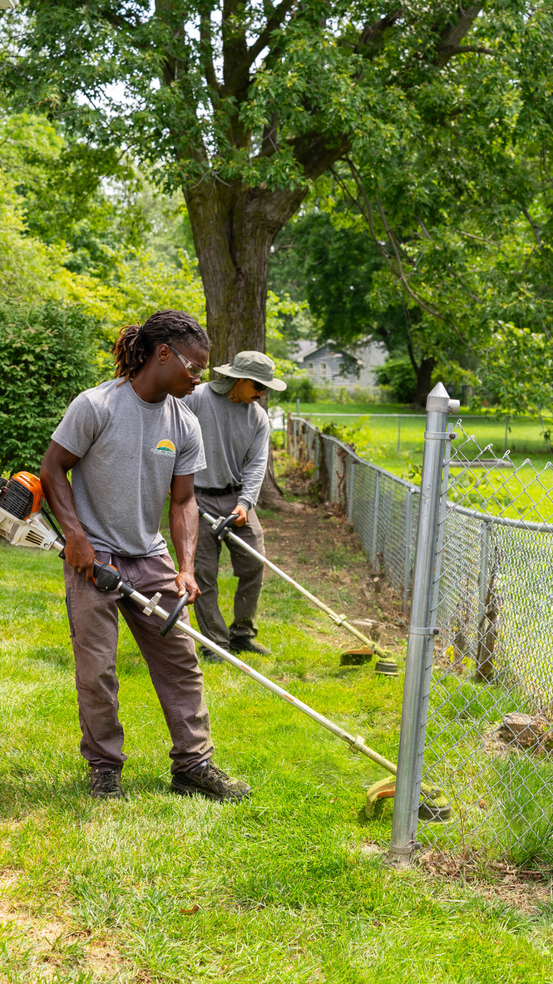 Two Heartland Grounds crew members trimming along a back yard fence line